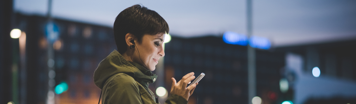 Jovem mulher utilizando o celular em rua movimentada
