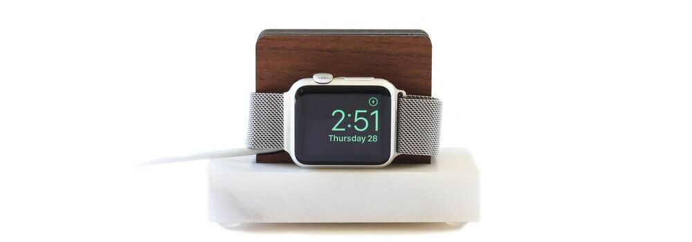 Smartwatch sobre uma base de madeira com fundo branco.