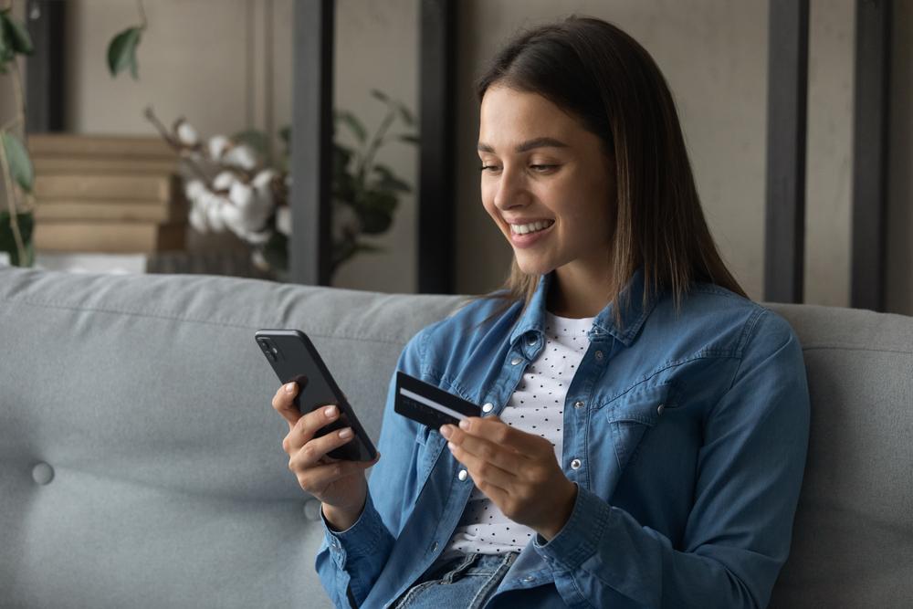 Mulher segurando celular e cartão com as mãos enquanto olha para a tela do celular